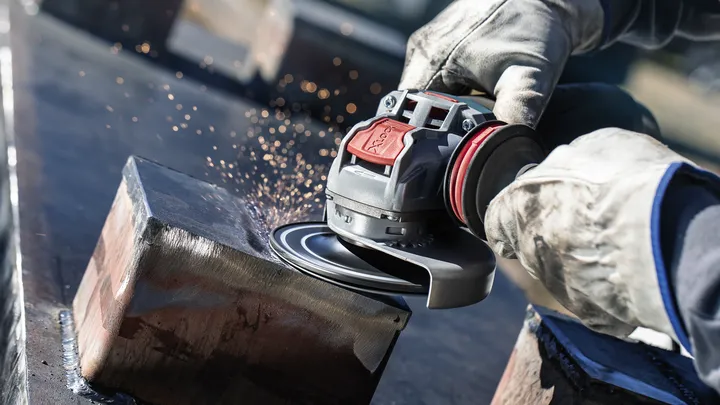 Güvenlik ekipmanı takan bir kişi açılı taşlama makinesiyle metal bir kirişi taşlıyor.