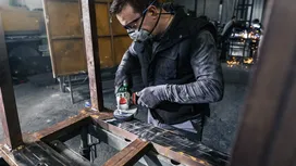İş güvenliği ekipmanı takan bir kişi atölyede metal kirişleri taşlıyor.