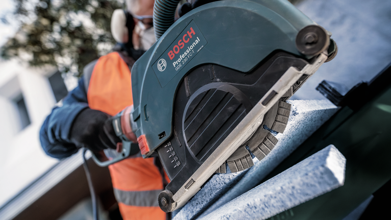 Güvenlik ekipmanı takan bir kişi, bir taş levhayı kesmek için elektrikli testere kullanıyor.