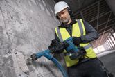 Güvenlik ekipmanı takan bir işçi, beton duvara akülü yıkım çekici kullanıyor.