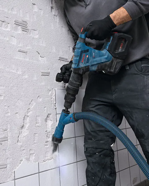 Güvenlik ekipmanı takan bir kişi, duvar karolarını kırmak için akülü yıkım çekici kullanıyor.