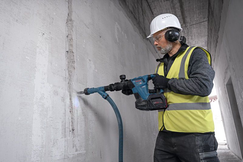 Güvenlik ekipmanı takan bir kişi, beton bir duvarı kırmak için akülü yıkım çekici kullanıyor.