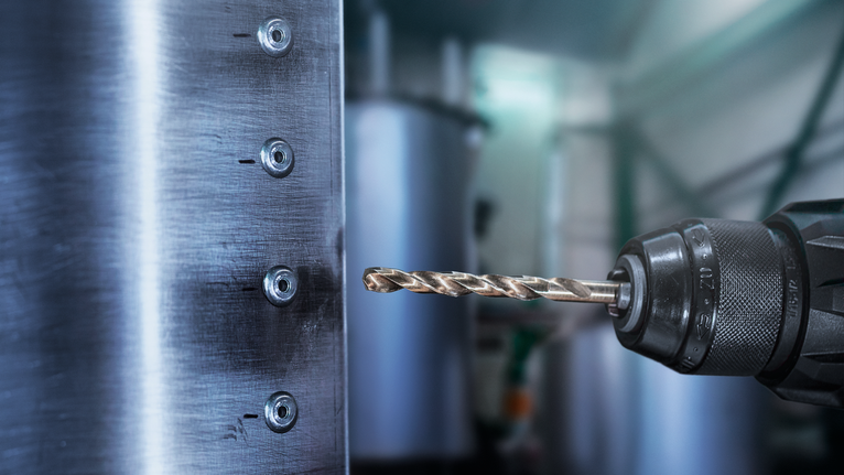 Endüstriyel bir atölyede metal levhaya delik açan elektrikli matkap.