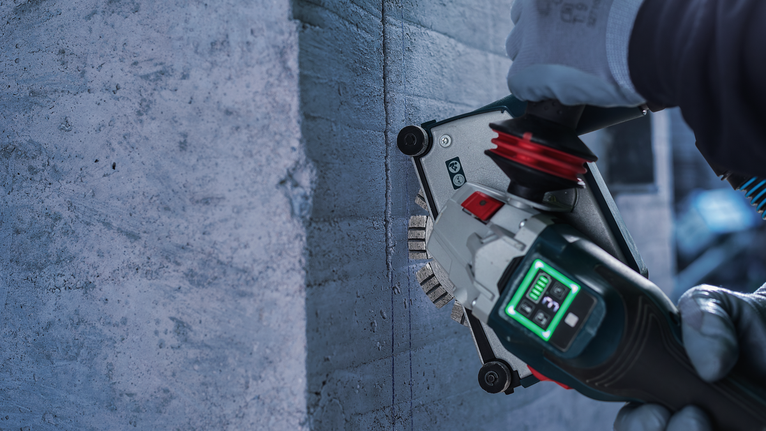 Güvenlik ekipmanı takan bir kişi, beton bir duvara oluk açmak için elektrikli alet kullanıyor.