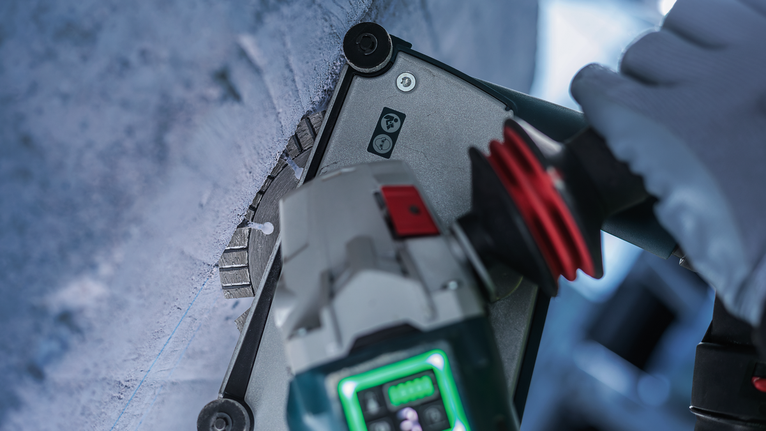 Güvenlik ekipmanı takan bir kişi elektrikli aletle beton duvara delik açıyor.