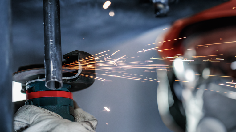 Güvenlik ekipmanı kullanan işçi metal boruyu öğütüyor, kıvılcım çıkıyor.