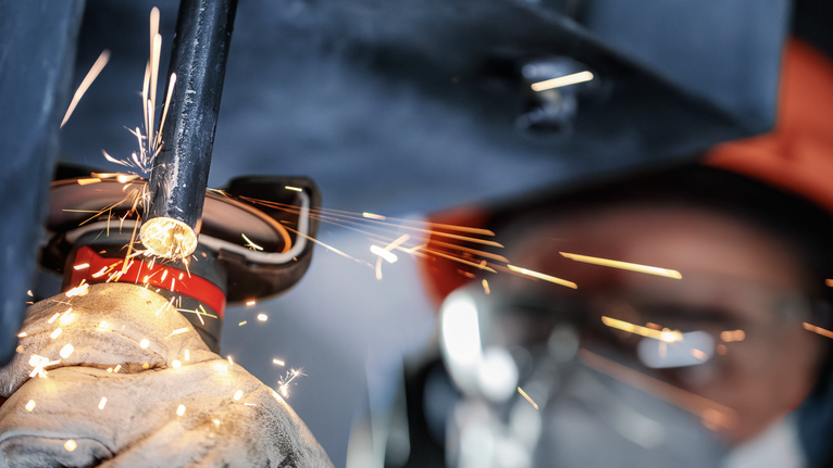 Güvenlik ekipmanı takan bir kişi metal boruyu öğütüyor ve parlak kıvılcımlar çıkıyor.