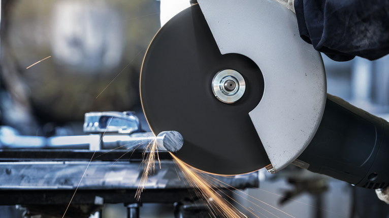 Güvenlik ekipmanı takan bir kişi, kıvılcımlar saçarak metali kesmek için büyük açılı taşlama makinesi kullanıyor.