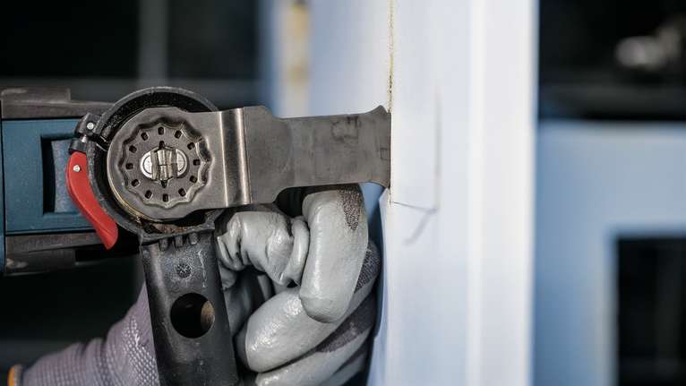 Güvenlik ekipmanı takan kişi, bir duvarı kesmek için elektrikli alet kullanıyor.