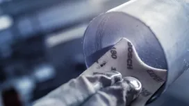 Güvenlik ekipmanı takan bir kişi metal borunun içini zımparalıyor.