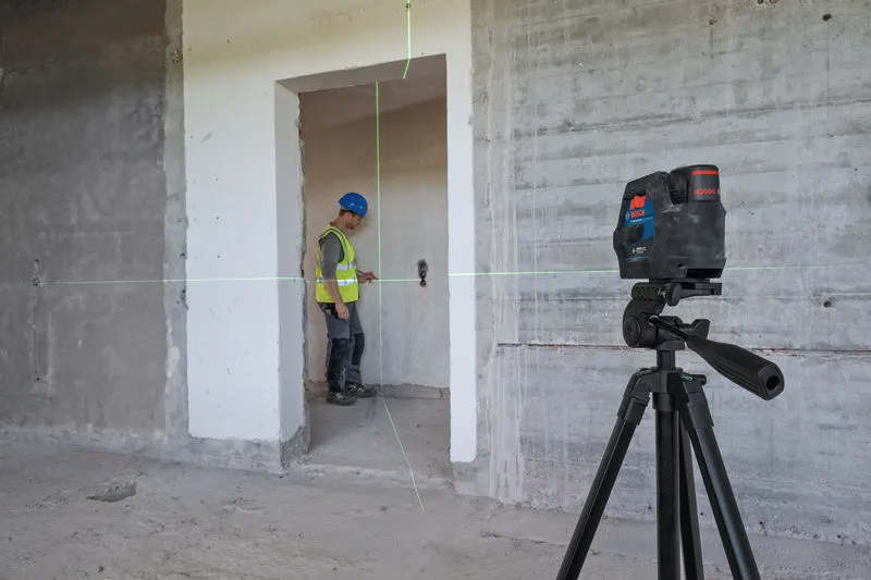 Güvenlik ekipmanı takan bir kişi, bir tripod üzerindeki lazer tesviye aletini kullanarak bir kapıyı hizalıyor.