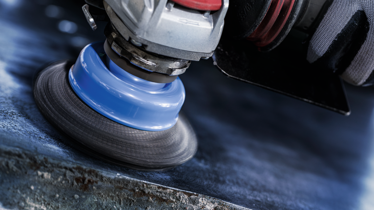 Güvenlik ekipmanı takan bir kişi, elektrikli aletle metal bir yüzeyi parlatıyor.