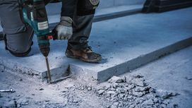 Güvenlik ekipmanı takan bir kişi beton zeminde yıkım matkabı kullanıyor.