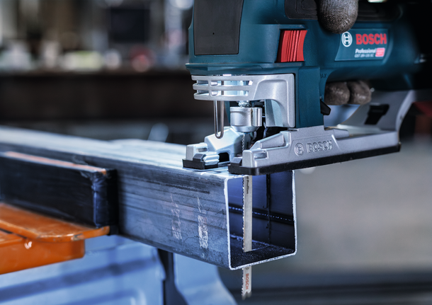 Güvenlik ekipmanı takan bir kişi, dekupaj testeresiyle metal bir kirişi kesiyor.