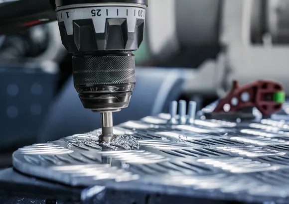 Metal talaşlarıyla çevrili metal bir iş parçasında hassas delikler açan matkap.