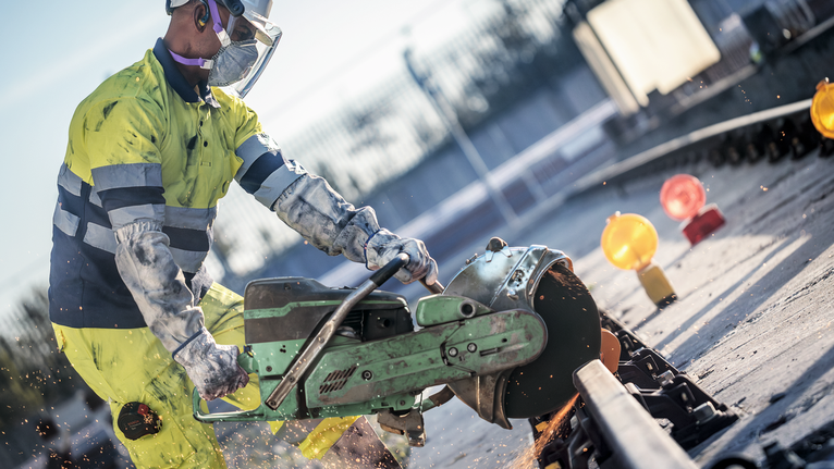 Güvenlik ekipmanı takan bir işçi, büyük bir elektrikli testere kullanarak çelik rayı kesiyor.