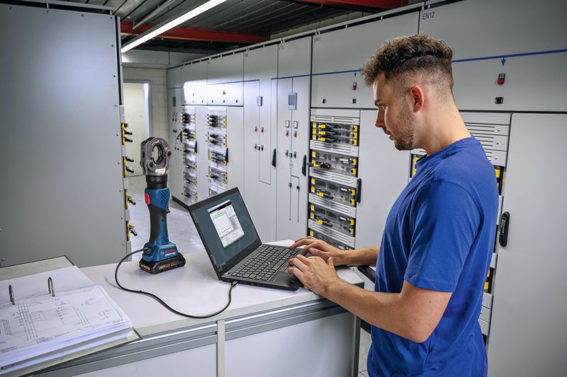 Kişi, elektrik kontrol odasında kablosuz hidrolik sıkma aletine bağlı bir dizüstü bilgisayarı çalıştırıyor.