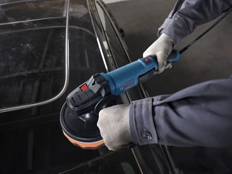 Güvenlik ekipmanı takan bir kişi, elektrikli parlatıcıyla bir arabanın tavanını parlatıyor.