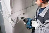 Güvenlik ekipmanı takan bir kişi beton duvara dairesel bir delik açıyor.