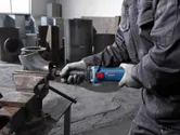 İş güvenliği ekipmanı takan bir kişi, atölyede düz taşlama makinesiyle metal bir boruyu taşlıyor.