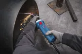 Güvenlik ekipmanı takan bir kişi, metal bir borunun kenarını taşlamak için düz bir taşlama makinesi kullanıyor.