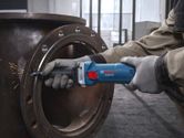Güvenlik ekipmanı takmış bir kişi düz bir taşlama makinesiyle metal bir boruyu taşlıyor.