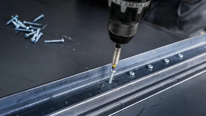 Bir çalışma tezgahında metal bir kirişe vidayı çakan elektrikli matkap.