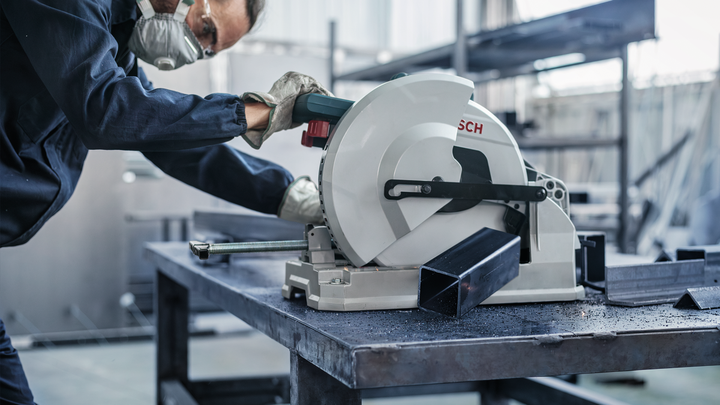 Güvenlik ekipmanı takan bir işçi dairesel testereyle metal bir kirişi kesiyor.