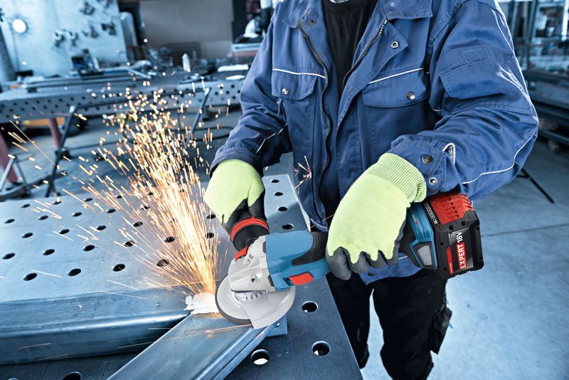Güvenlik ekipmanı takan bir kişi, akülü açılı taşlama makinesiyle metali taşlıyor.
