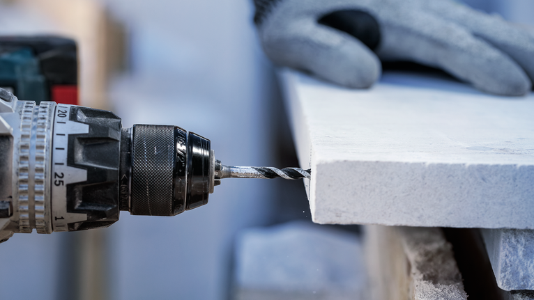 Güvenlik ekipmanı takan bir kişi taş levhaya delik açıyor.