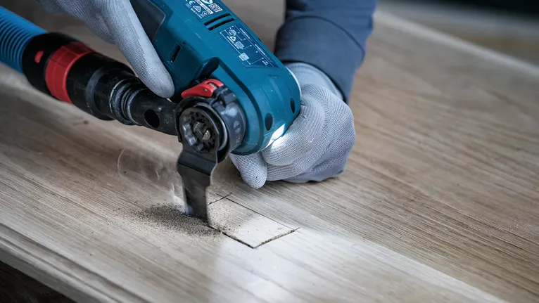 Güvenlik ekipmanı takan bir kişi, elektrikli aletle tahtada dikdörtgen bir delik açıyor.