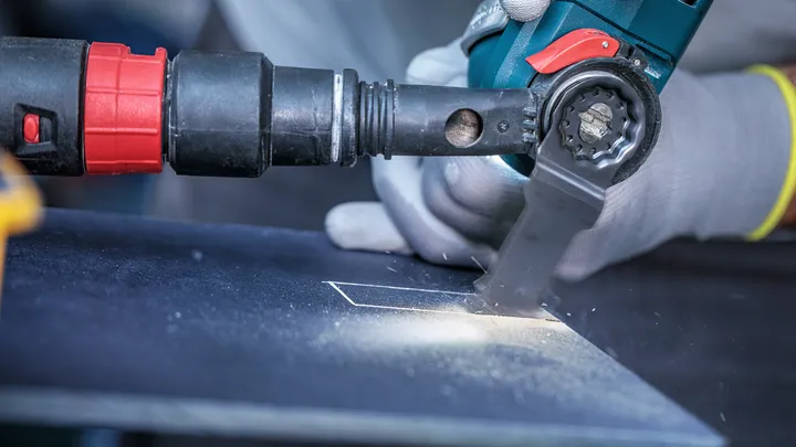 Güvenlik ekipmanı takan kişi, metal bir sacda hassas bir dikdörtgen kesmek için elektrikli bir alet kullanıyor.