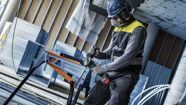 Bir inşaat alanında güvenlik ekipmanı takan bir kişi metal bir boruyu delmektedir.