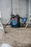 Şantiye zemininde duran kablosuz sırt çantası tipi toz emme makinesi.