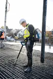 Güvenlik ekipmanı giyen bir kişi, demir donatı ızgarası üzerinde beton vibratörü kullanıyor.