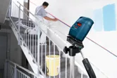 Laser leveling tool projects lines on a stairway wall while a person prepares the surface.