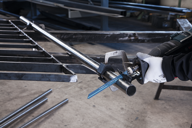 Worker wearing safety equipment uses a reciprocating saw to cut a metal pipe.