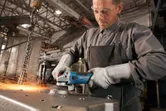 A person wearing safety equipment grinds metal with an angle grinder, producing sparks.