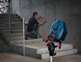 Person kneeling beside stairs uses a laser leveling tool projecting a red line on a concrete wall.