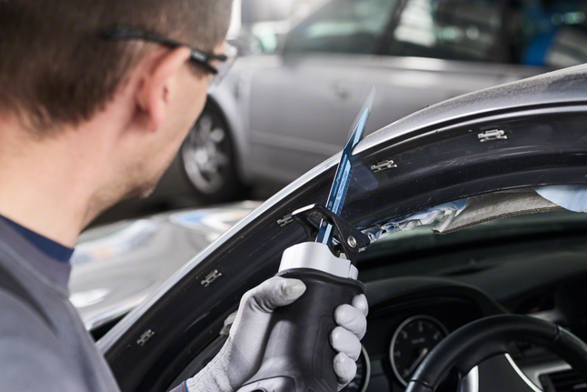 A worker wearing safety equipment uses a reciprocating saw to cut a car frame.
