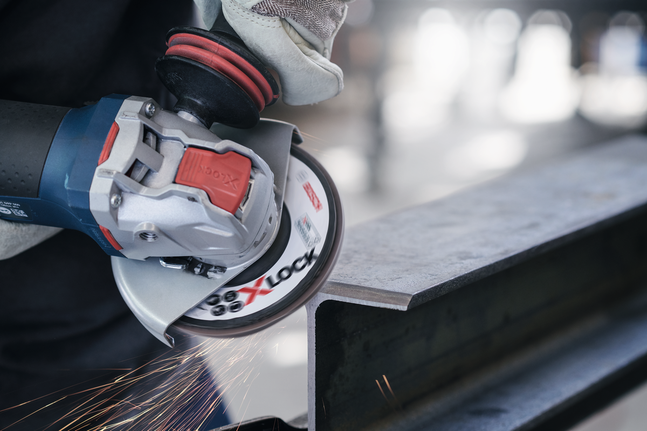 A person wearing safety equipment grinds a metal beam with a power tool, creating sparks.