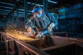 A person wearing safety equipment grinds metal, creating a shower of sparks.