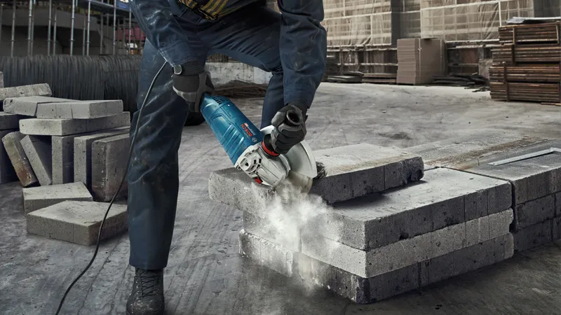A person wearing safety equipment cuts concrete blocks with a power cutter.