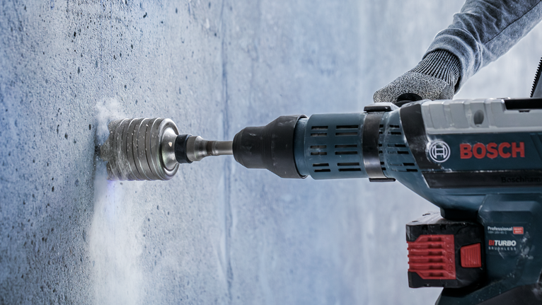 A person wearing safety equipment drills a hole into concrete with a power tool.