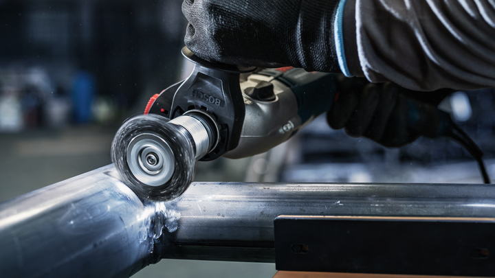 Person wearing safety equipment polishes a metal pipe with a power tool.
