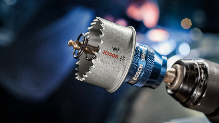 A hole saw attachment connected to a power drill in a workshop setting.