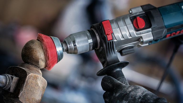 Person wearing safety equipment polishes a wooden sphere using a rotary power tool.