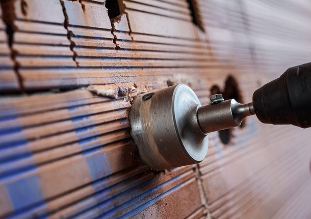 Hole saw drilling into a tiled wall to create an opening.