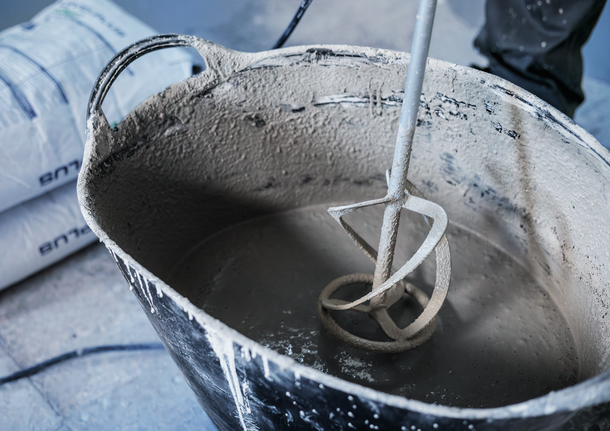 A person wearing safety equipment mixes cement in a large tub with a paddle mixer.