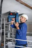 A person wearing safety equipment uses a cordless concrete nailer to fasten material to a ceiling.